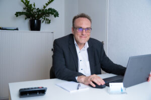 Philippe Bally arbeitet konzentriert am Computer und lächelt freundlich in die Kamera